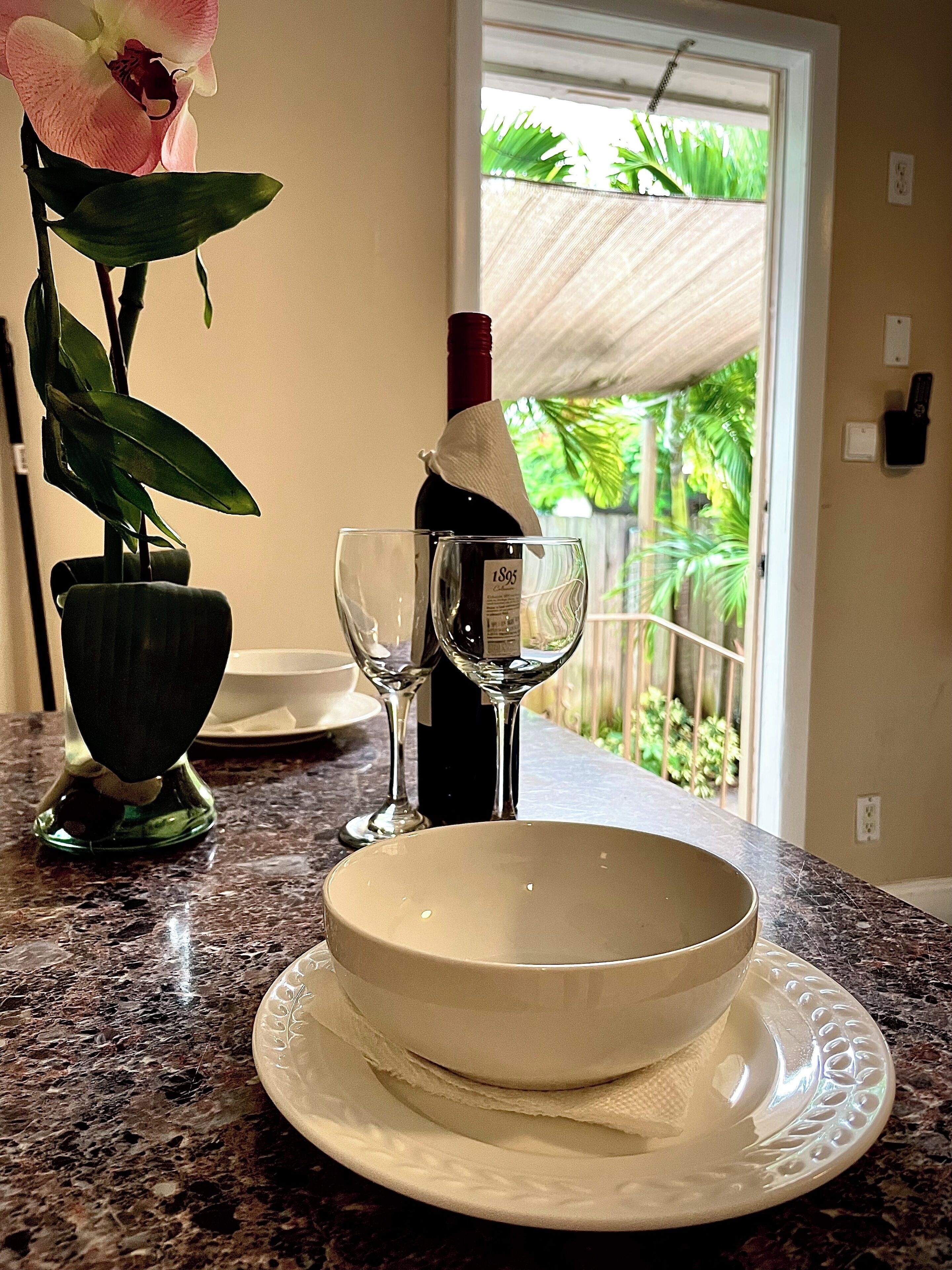 A kitchen counter with a wine bottle, two glasses, and a bowl set.