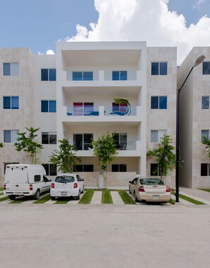 Un immeuble moderne à plusieurs étages, doté d’une façade plate, de balcons et d’un espace de stationnement pouvant accueillir trois voitures et un fourgon.