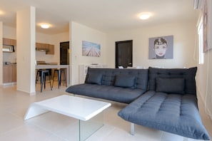 Un salon moderne avec un canapé d’angle gris, une table basse blanche et une cuisine en arrière-plan.