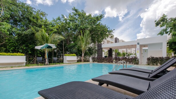 Una piscina con lettini e una zona coperta, immersa nel verde e circondata da architettura moderna.