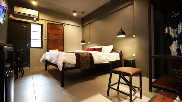 Habitación de hotel moderna con cama, escritorio y una silla. Se ve una ventana con persianas, un aire acondicionado de pared y un perchero.