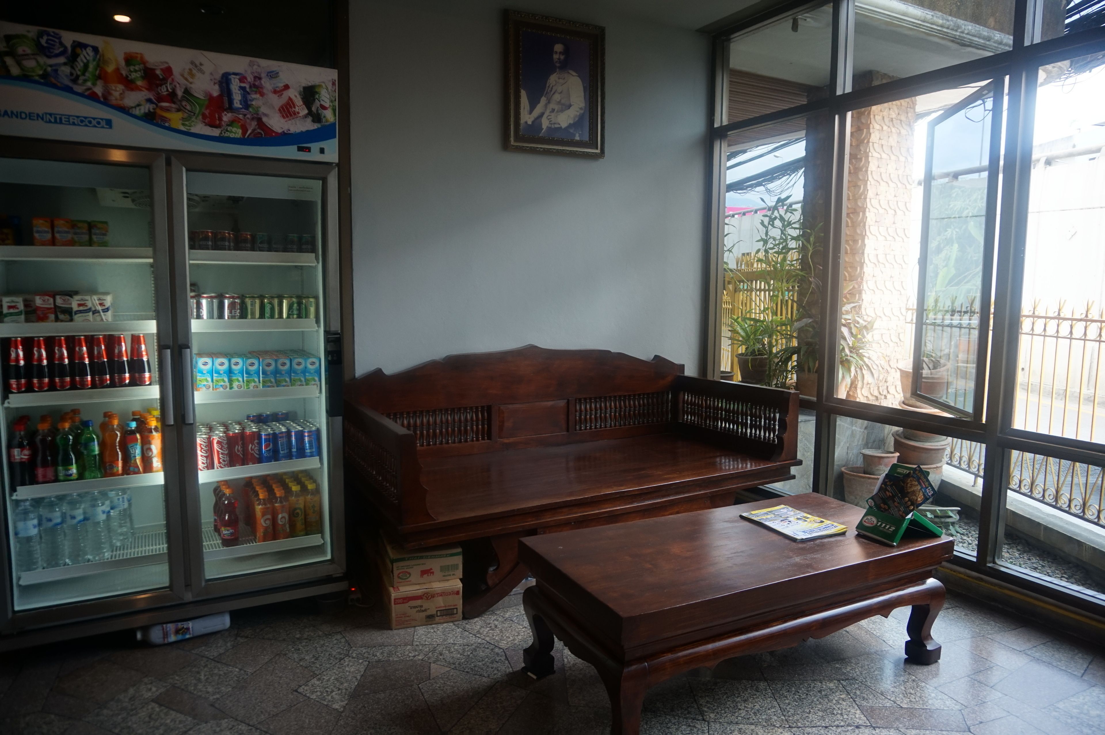 A room with a wooden bench and a table, a beverage refrigerator stocked with drinks, and a large window with a view of the outside.