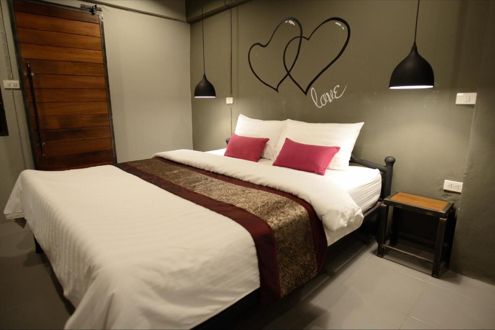 A bedroom with a large bed, two bedside tables, a wooden door, and a wall with a heart design and the word "love".