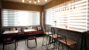 Un comedor moderno con una mesa de madera, sillas negras y un banco. Hay ventanas grandes con persianas, y un candelabro cuelga del techo.