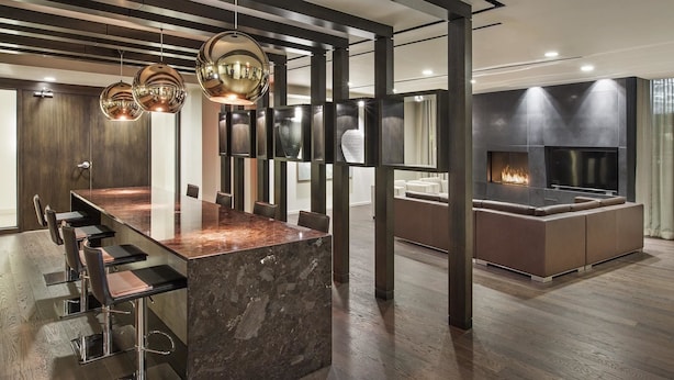 Une cuisine moderne dotée d’un îlot en marbre, de tabourets de bar, de luminaires suspendus et d’une cheminée intégrée.
