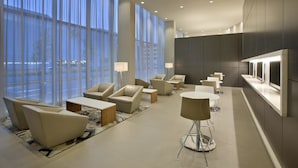 Un hall d’hôtel moderne, doté de grandes fenêtres, de sièges confortables et d’un espace de réception.