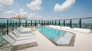 Une piscine sur le toit, dotée de rampes en verre, de chaises longues et offrant une vue dégagée sur le paysage urbain.