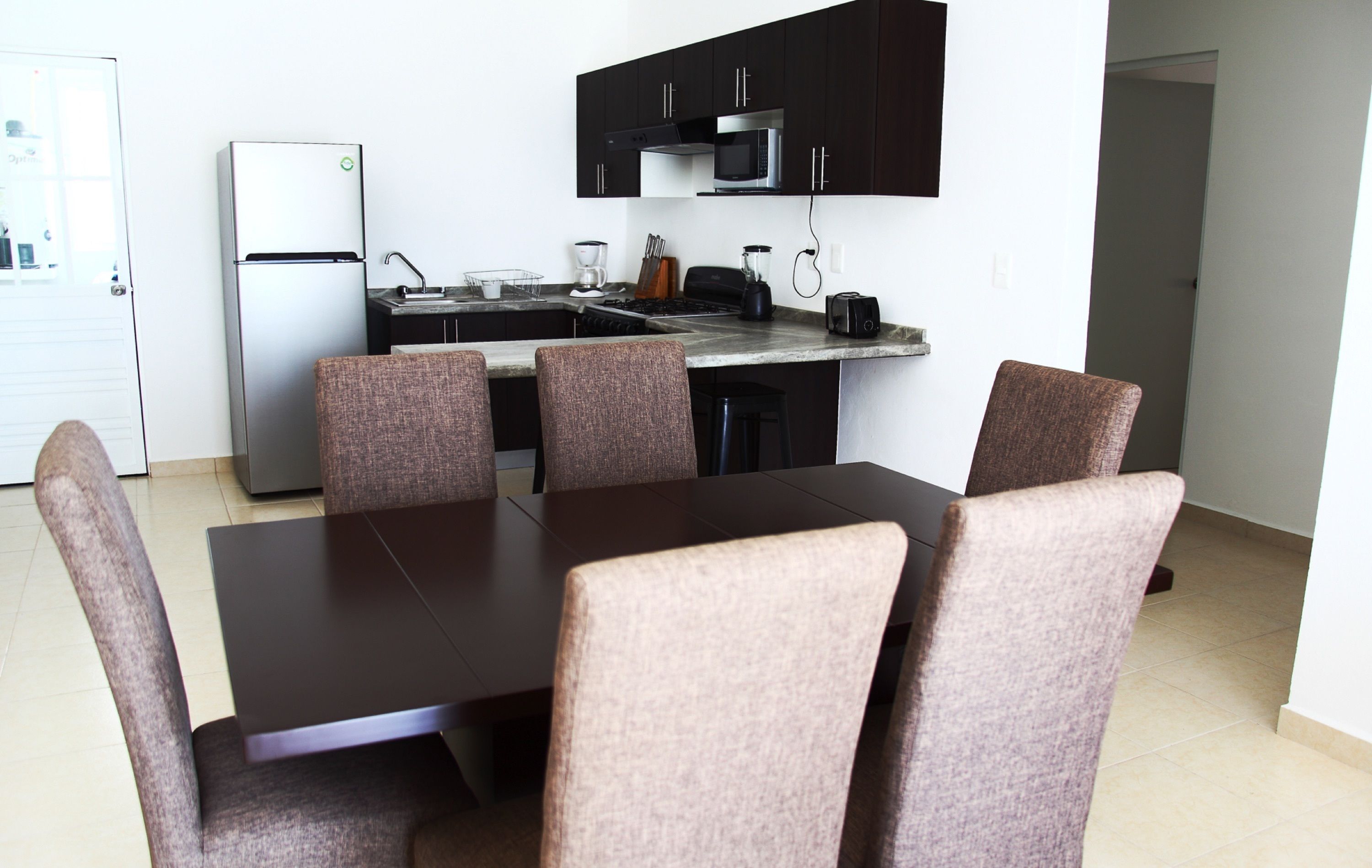 A compact kitchen with a refrigerator, microwave, and stove. There is a dining table with four chairs.