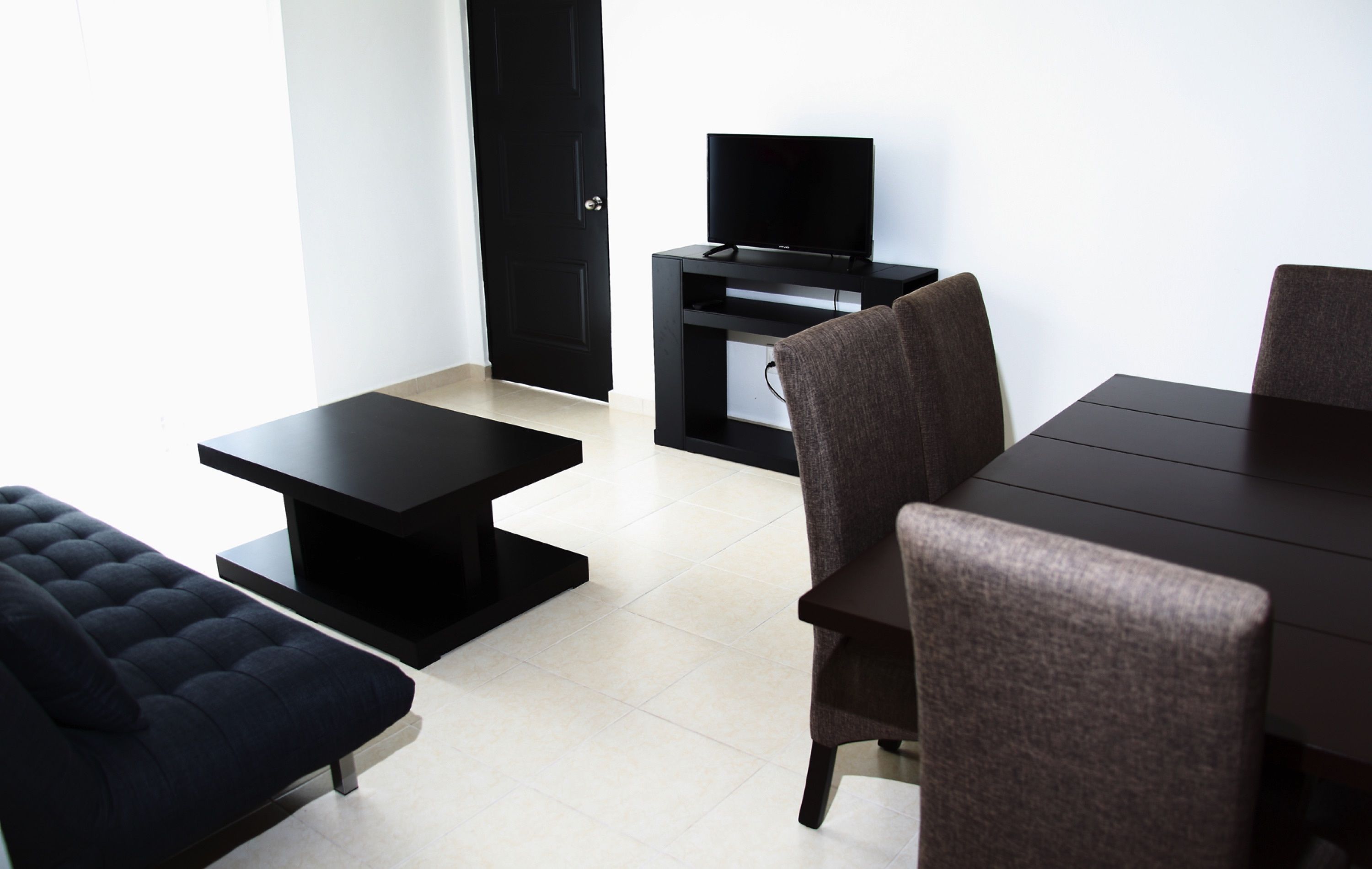 Un salon moderne avec un canapé marron foncé, une table basse noire, un téléviseur posé sur un meuble et une table à manger avec des chaises.