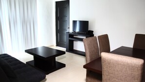 Een moderne woonkamer met een zwarte bank, een salontafel, een tv op een meubel en een eettafel met stoelen.