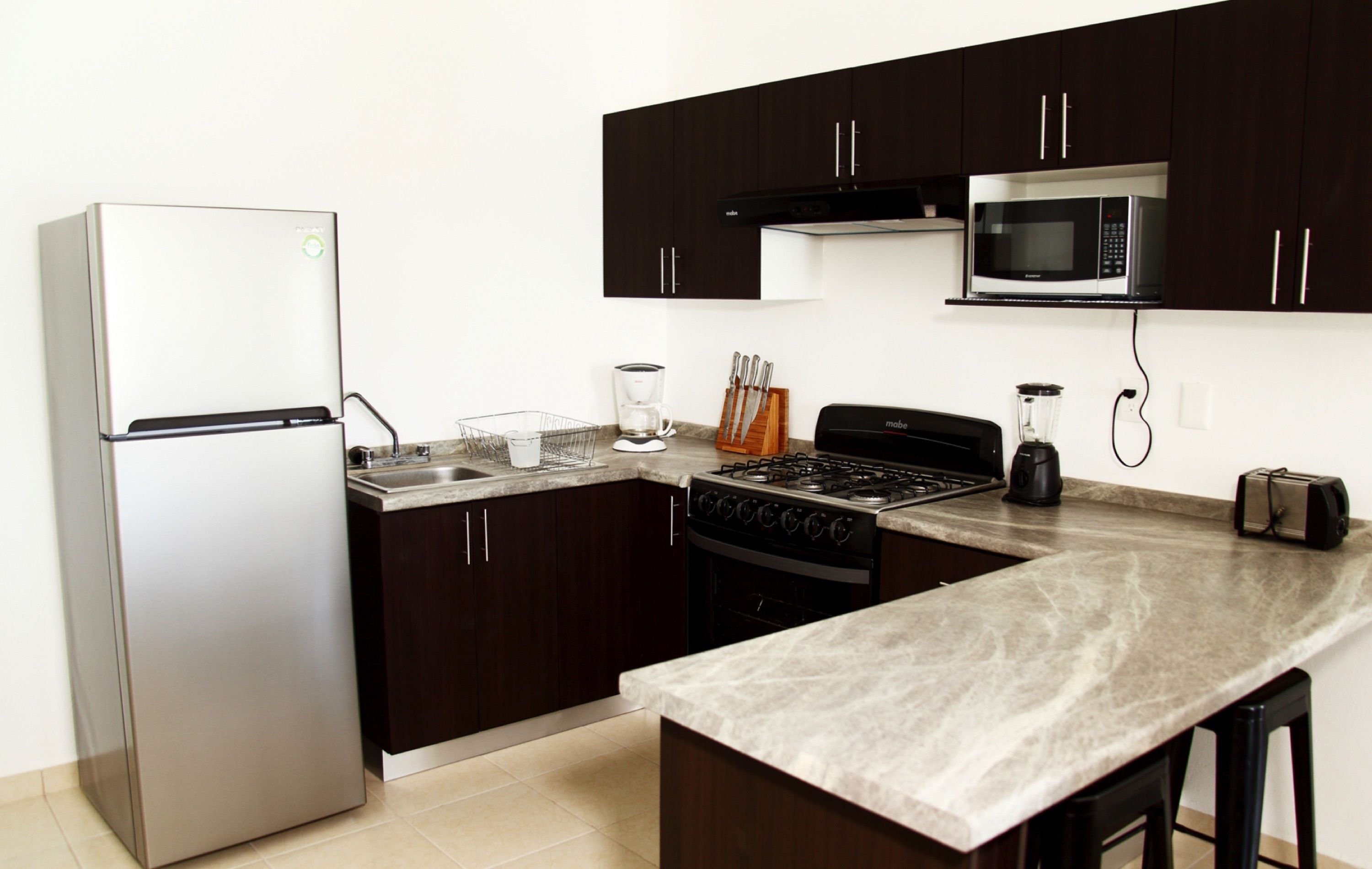 A modern kitchen with dark cabinets, stainless steel appliances, and a marble countertop.