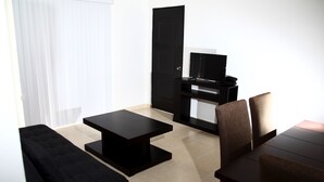 Een moderne woonkamer met een zwarte bank, een zwarte salontafel, een tv-meubel met een flatscreen-tv en een deur.