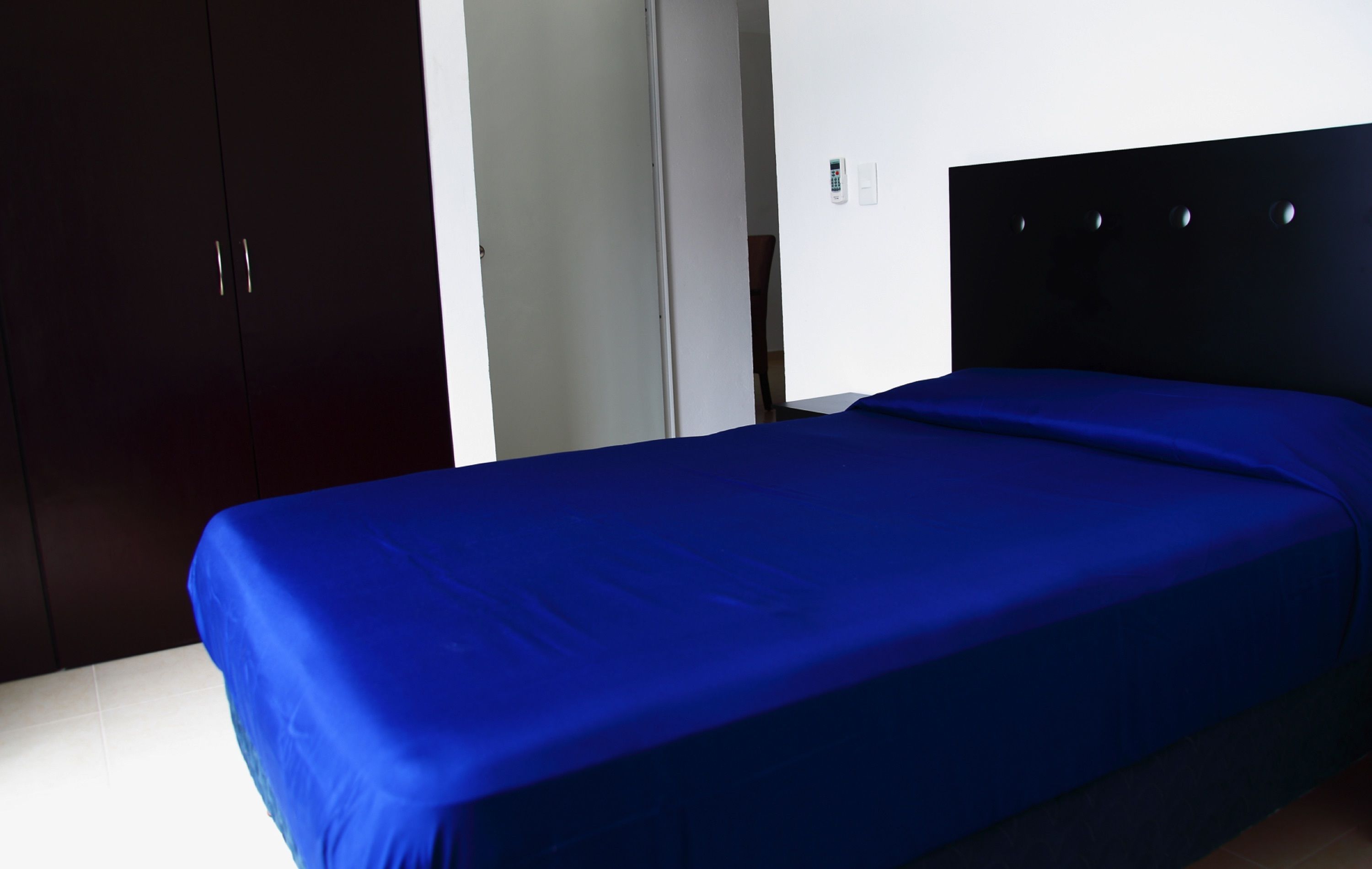 Una cama individual con una colcha azul en una habitación con armarios de madera oscura y una pared blanca.