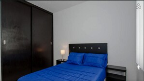 A bedroom with a bed, a nightstand, a lamp, and a wardrobe. - DEPARTAMENTO VELAS SELVANOVA 512 (Playa del Carmen)