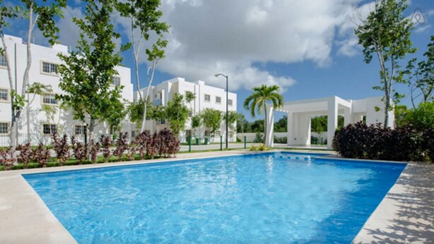 A swimming pool with a clear blue water surface, surrounded by white buildings and greenery. - DEPARTAMENTO VELAS SELVANOVA 512 (Playa del Carmen)