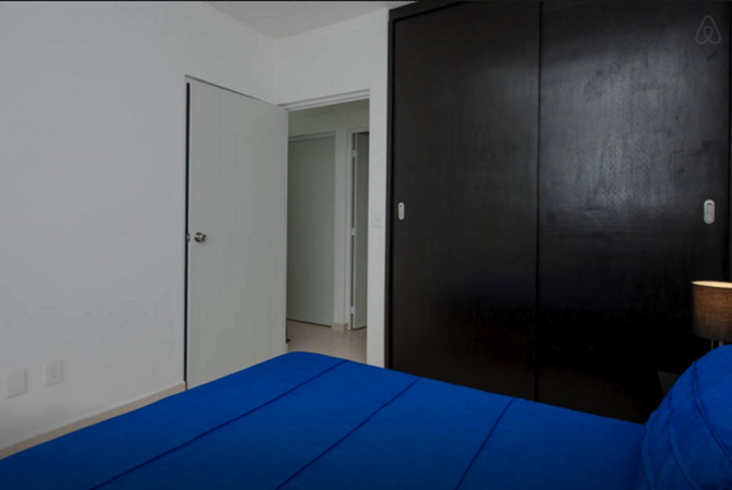 A room with a bed, a wardrobe, and a door leading to another room.