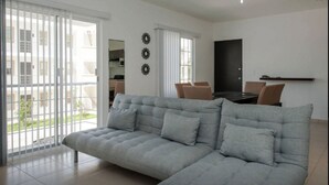 A modern living room with a grey sectional sofa, a dining table with chairs, and a TV on the wall. - DEPARTAMENTO VELAS SELVANOVA 512 (Playa del Carmen)
