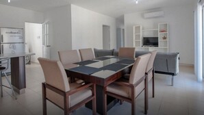 A modern dining area with a glass-top table, cushioned chairs, and a built-in TV shelf. - DEPARTAMENTO VELAS SELVANOVA 512 (Playa del Carmen)