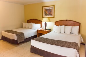 A hotel room with two beds, each with a wooden headboard, a bedside table with a lamp, and a framed artwork on the wall.