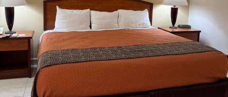 A hotel room with a large bed, two bedside tables with lamps, and a plain wall.