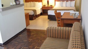 A hotel room with a bed, a sitting area with a patterned sofa, a wooden table, and a small desk.