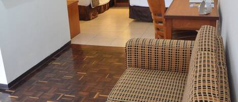 A hotel room with a bed, a sitting area with a patterned sofa, a wooden table, and a small desk.