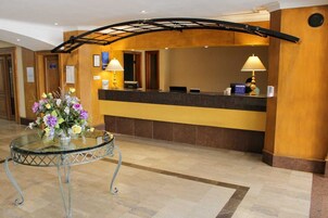 A szálloda recepciós területe, amelyben található egy recepciós pult, egy virágdíszítéssel ellátott üvegasztal és egy ívelt mennyezeti szerkezet.