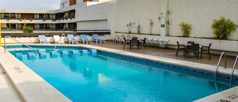 A rectangular swimming pool with blue water, surrounded by lounge chairs and tables.