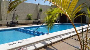 A swimming pool with blue tiles, a palm tree, and outdoor furniture.