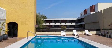 Piscina com espreguiçadeiras e um edifício com fachada amarela.
