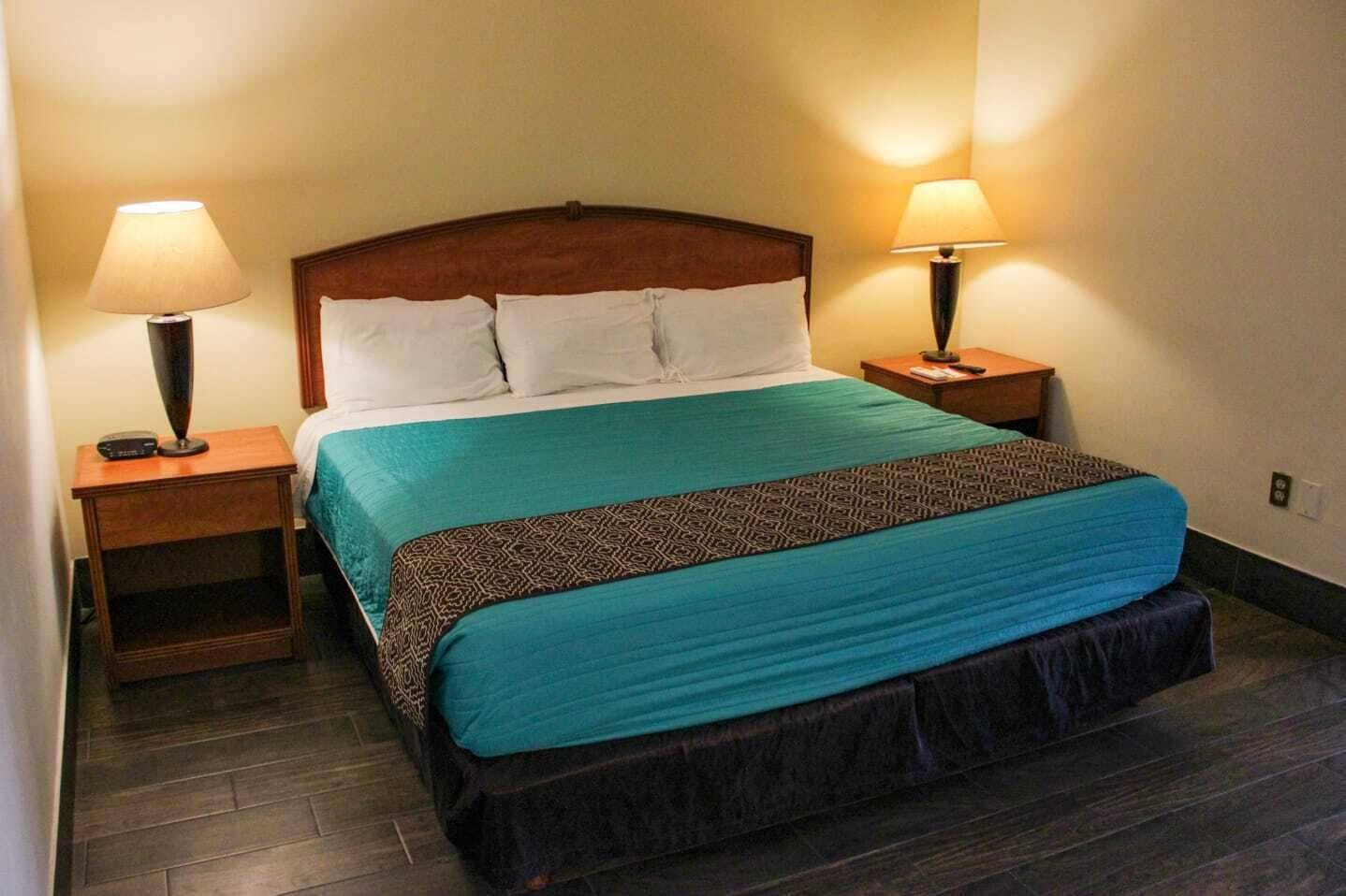 A neatly made bed with a patterned bedspread, two bedside tables with lamps, and a wooden headboard.
