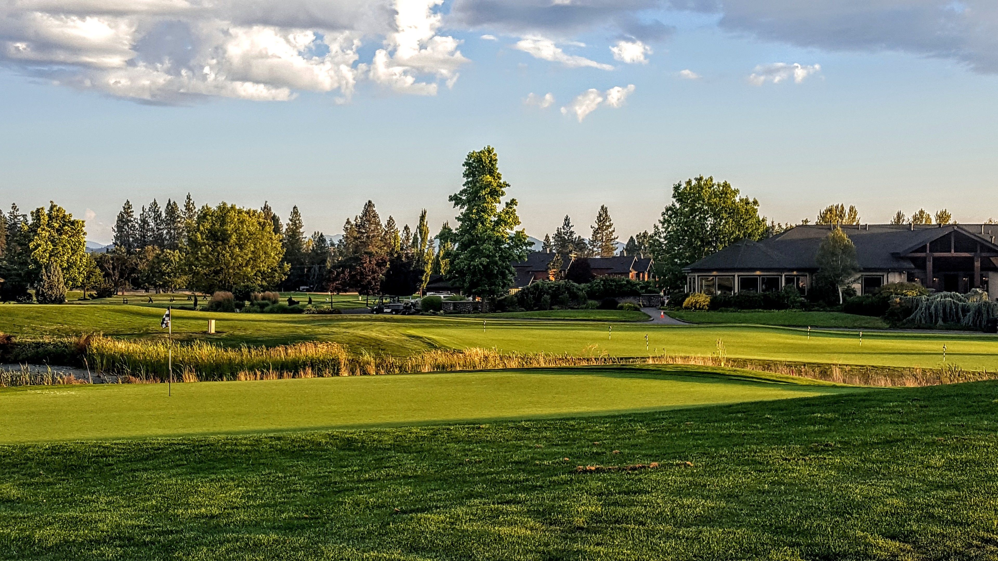 A golf course with a clubhouse, trees, and a pond.