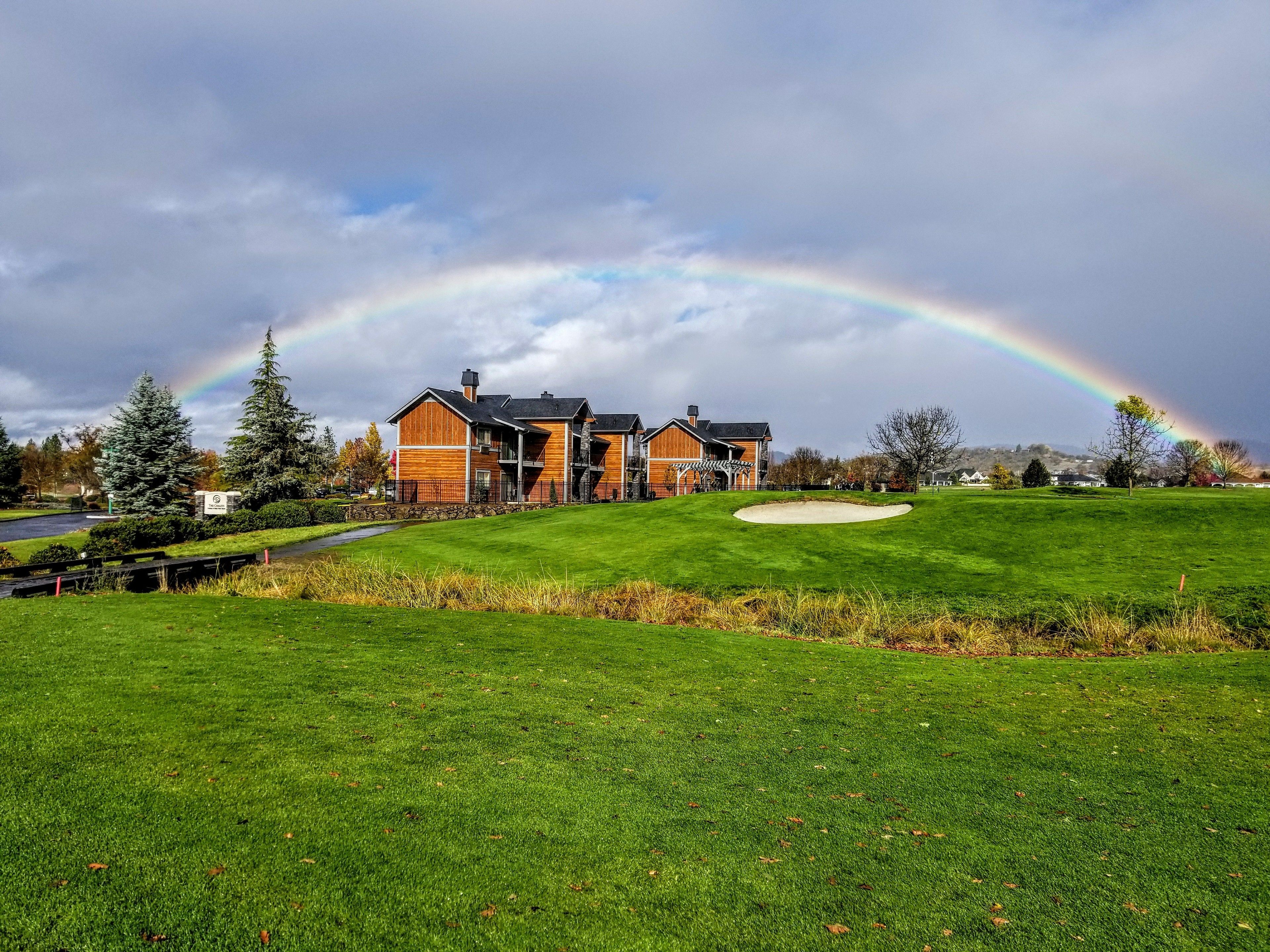 A golf course with a house in the background and a rainbow.