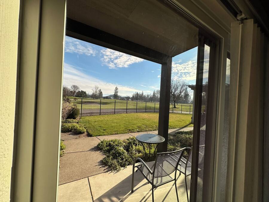 Un patio con mesa y sillas, vista a un parque con cerca y cielo despejado.