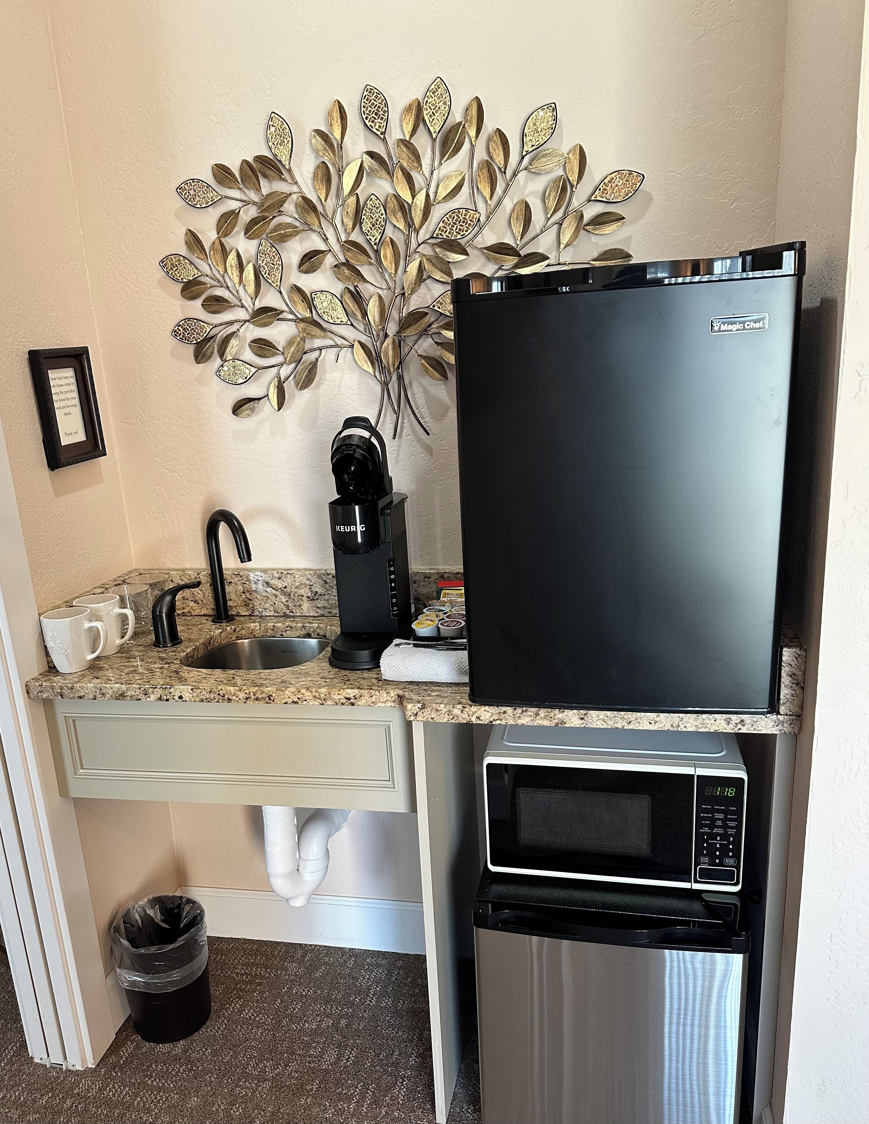 A compact kitchenette with a sink, coffee maker, refrigerator, and microwave.