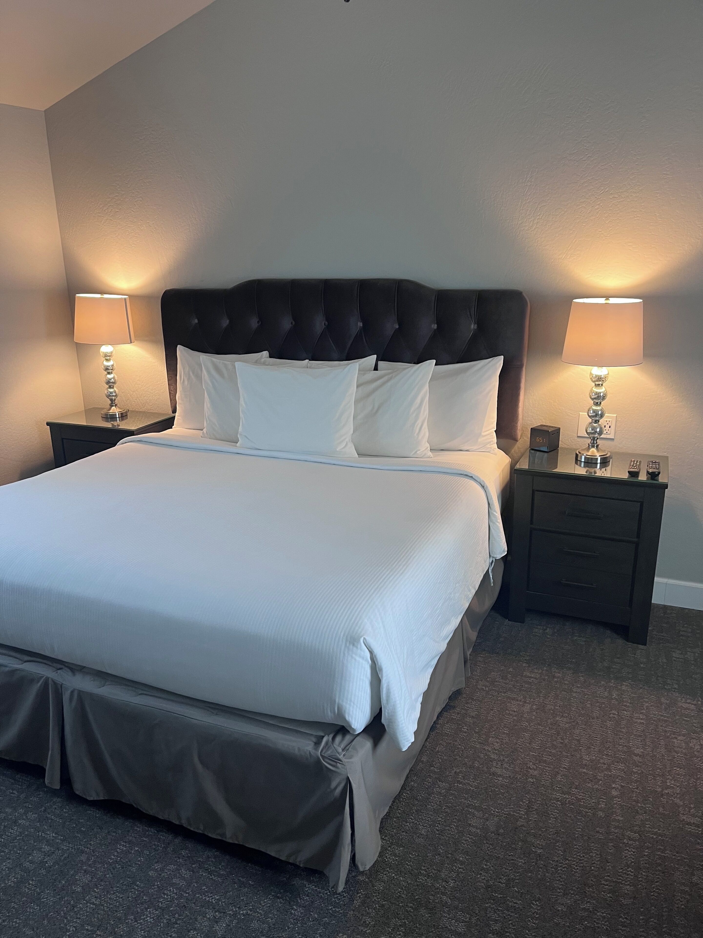 A neatly made bed with a tufted headboard, two bedside tables with lamps, and a carpeted floor.