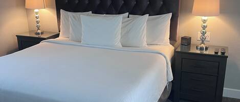 A neatly made bed with a tufted headboard, two bedside tables with lamps, and a carpeted floor.