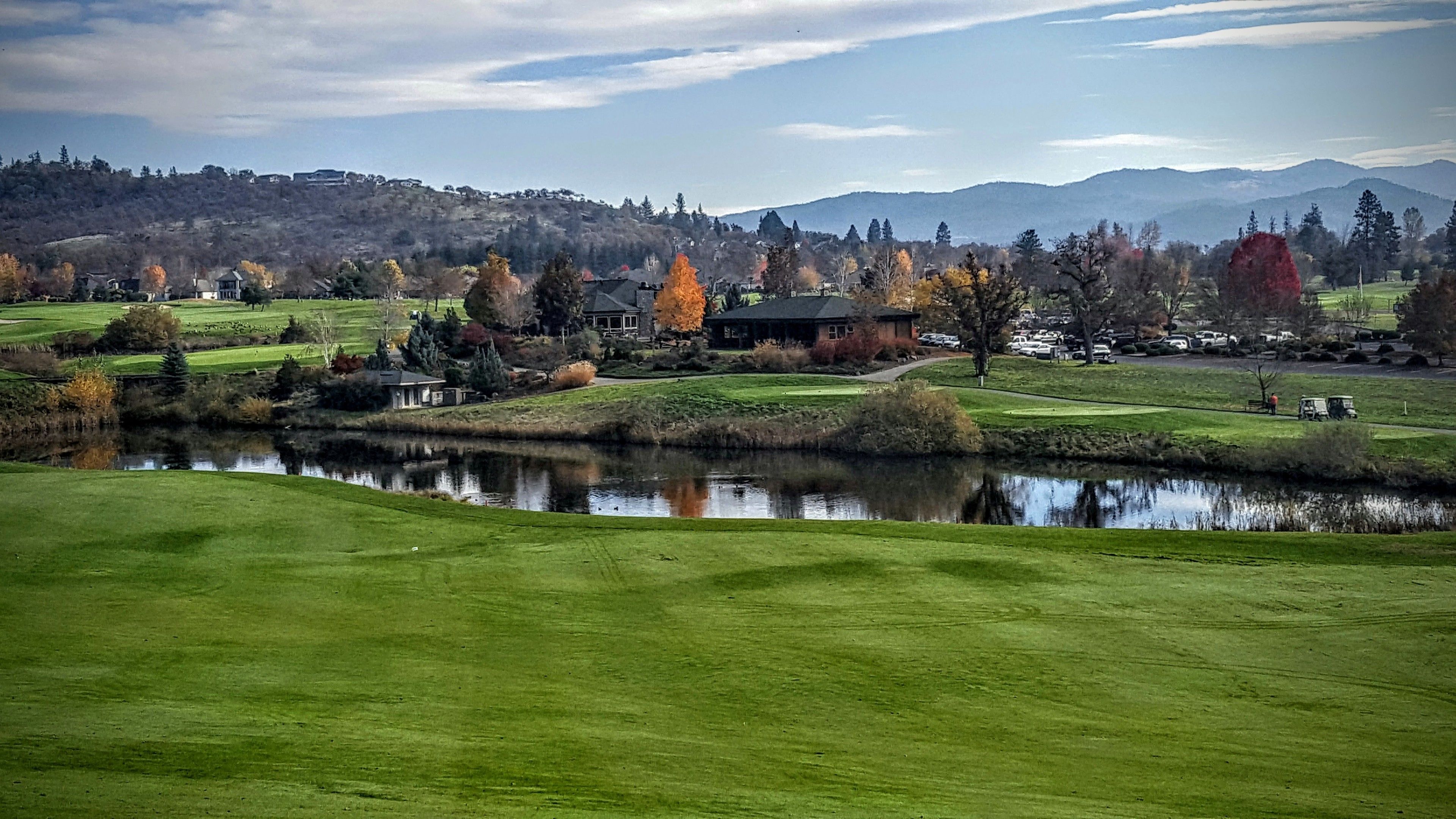 A golf course with a pond, houses, and a mountain range in the background.