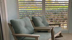 Una habitación con dos mecedoras y vistas a través de una ventana con persianas.