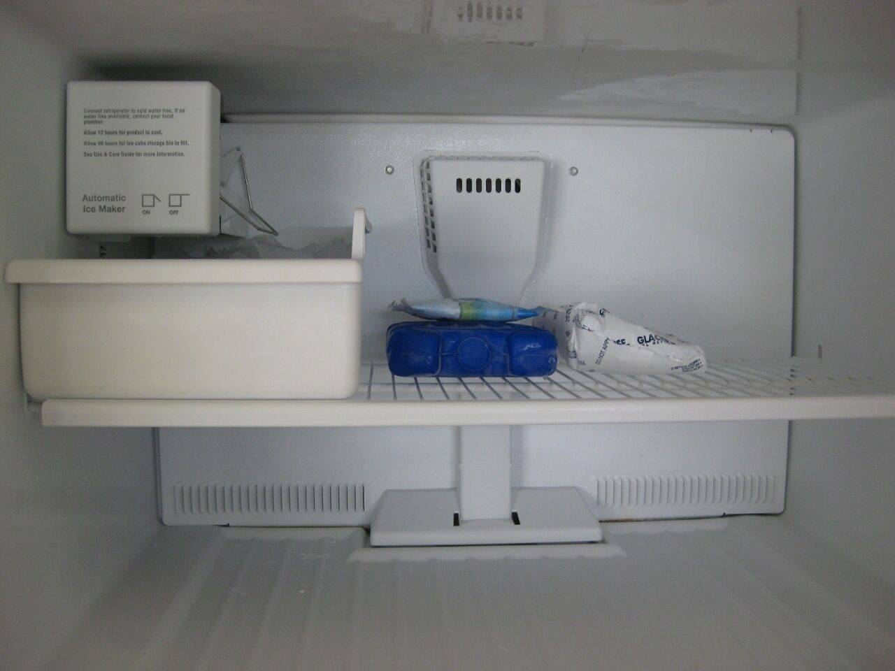 A refrigerator with an automatic ice maker, a water dispenser, and a shelf with a blue container and a bag of ice.
