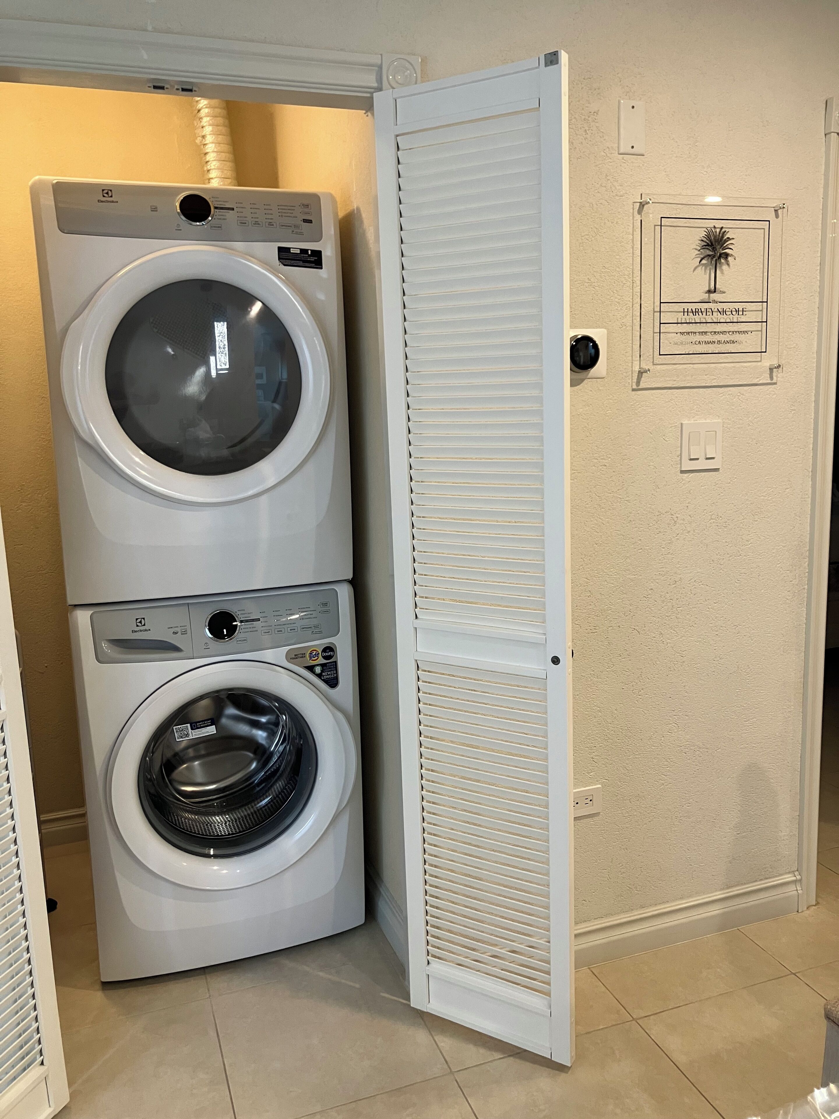 A laundry room with two stacked front-loading washing machines and a door with a plaque.