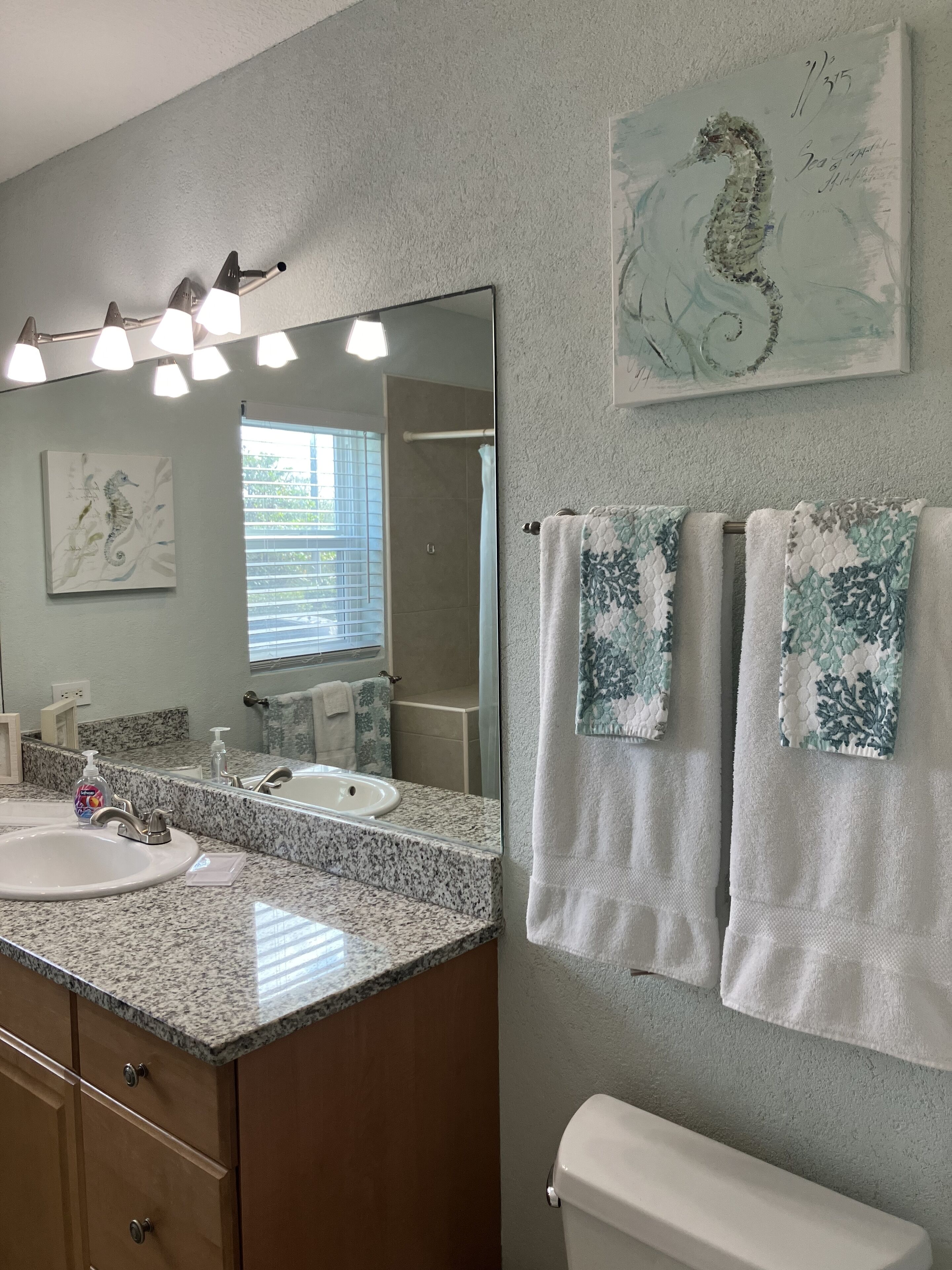A bathroom with a granite countertop sink, a large mirror, and two towels hanging on a towel rack.