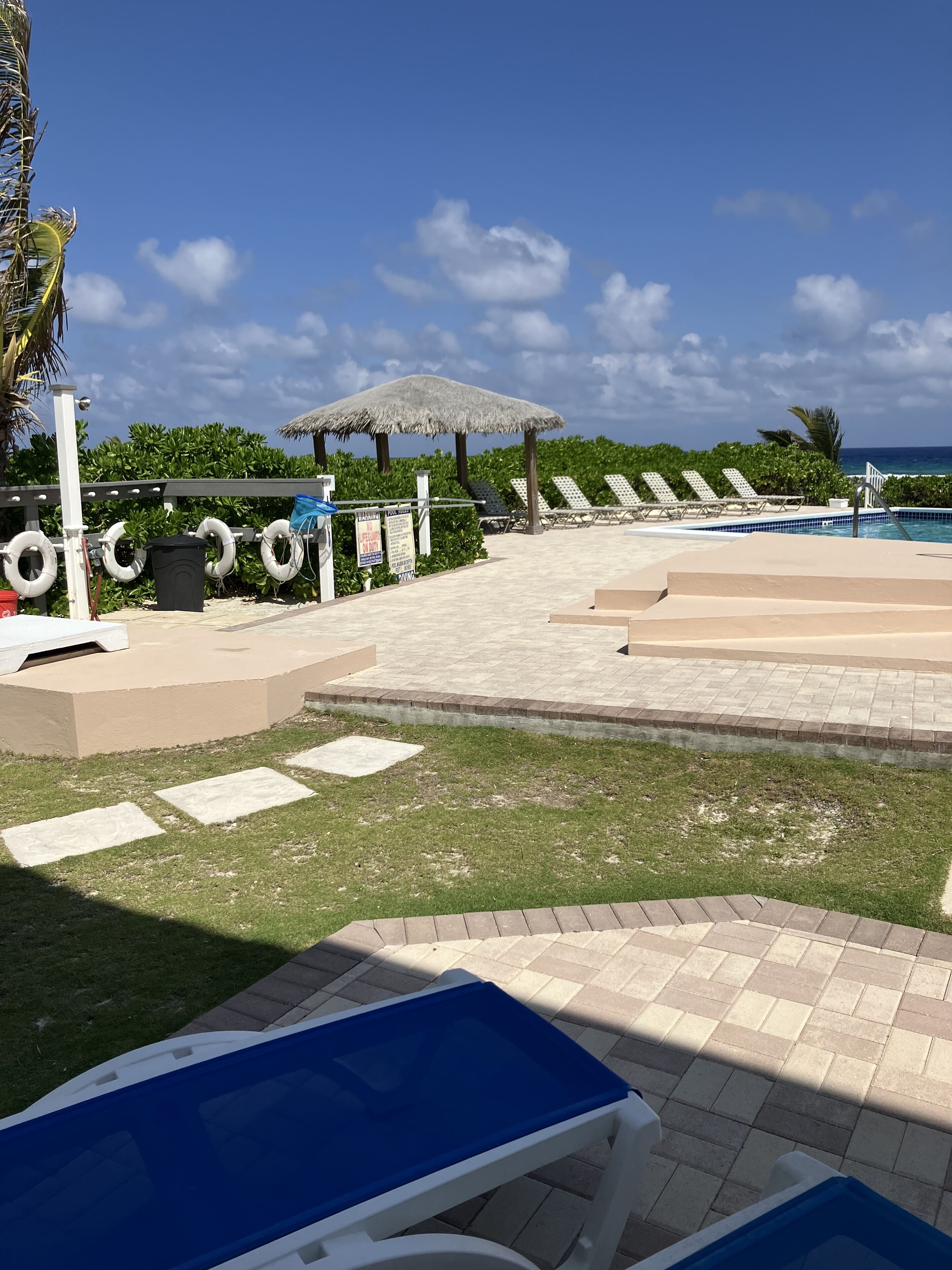Un espace aménagé au bord de la piscine, avec des chaises longues, un parasol en chaume et des bouées de sauvetage.