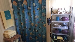 Un baño con cortina de ducha azul adornada con motivos de peces, un banco de madera, un perchero con toallas dobladas y un estante con distintos artículos de aseo.