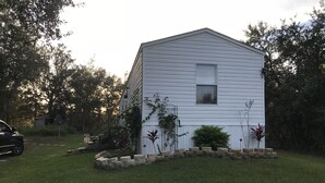 Una casa blanca de un solo piso con una pequeña ventana, rodeada de un césped cuidado y un borde de piedra.