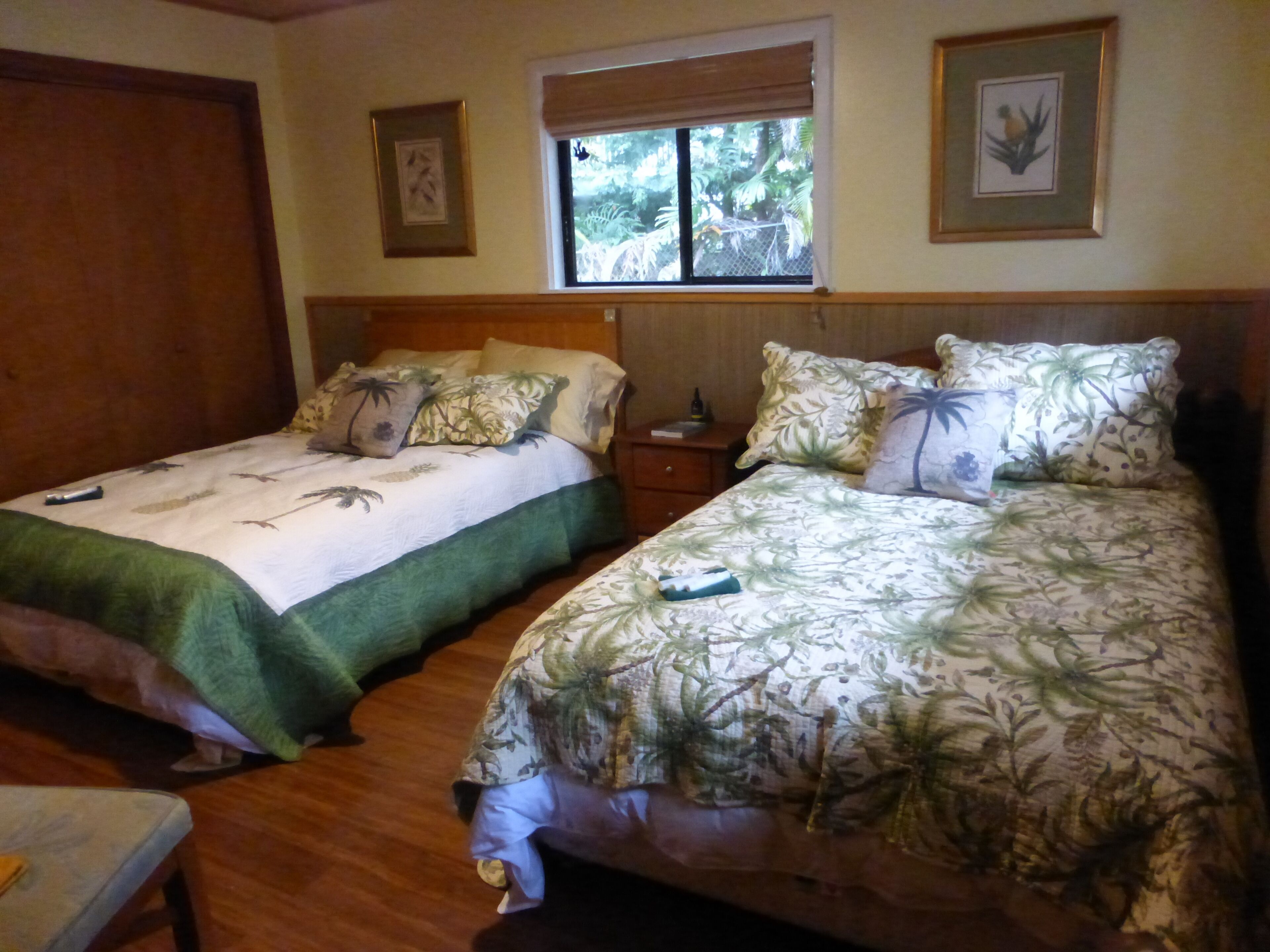 Une chambre avec deux lits, chacun recouvert d’une couvre-lit à motifs floraux et agrémenté d’oreillers. Une fenêtre offre une vue sur la verdure environnante.