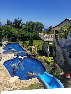 A swimming pool area with multiple pools, a slide, and a covered deck.