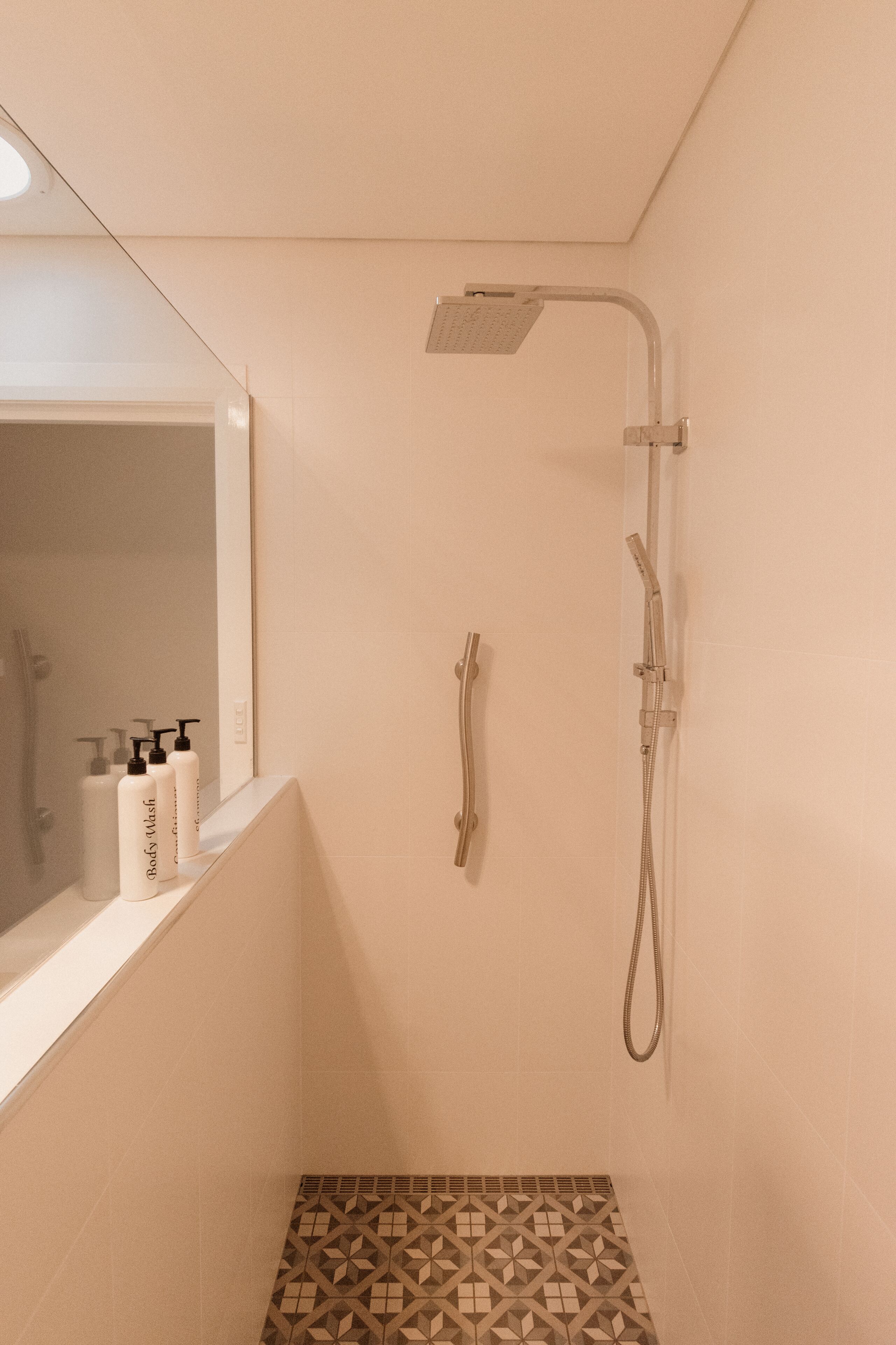 A bathroom with a shower, a mirror, and toiletries on the counter.