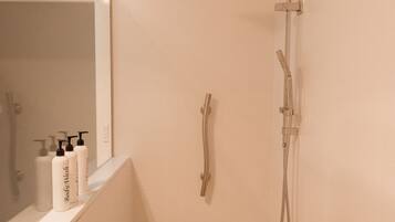 A bathroom with a shower, a mirror, and toiletries on the counter.