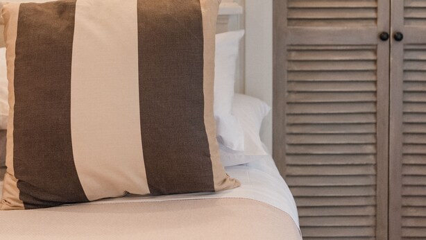 Ein Schlafzimmer mit einem Bett, einem gestreiften Kopfkissen, einem Nachttisch, einer Wandlampe und einem Holzschrank.
